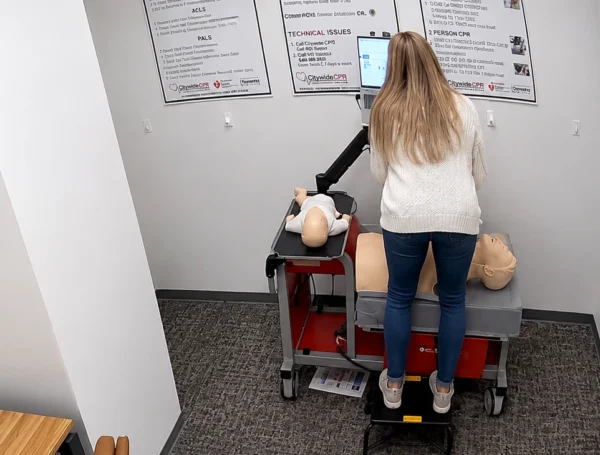 Participant using a laptop at a Citywide CPR simulation station in Arlington, Virginia, with adult and infant CPR manikins visible.