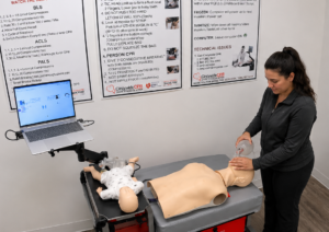 Participant providing bag-valve-mask ventilation to an adult CPR manikin at a Citywide CPR simulation station in Atlanta, Georgia, with an infant manikin and laptop visible.
