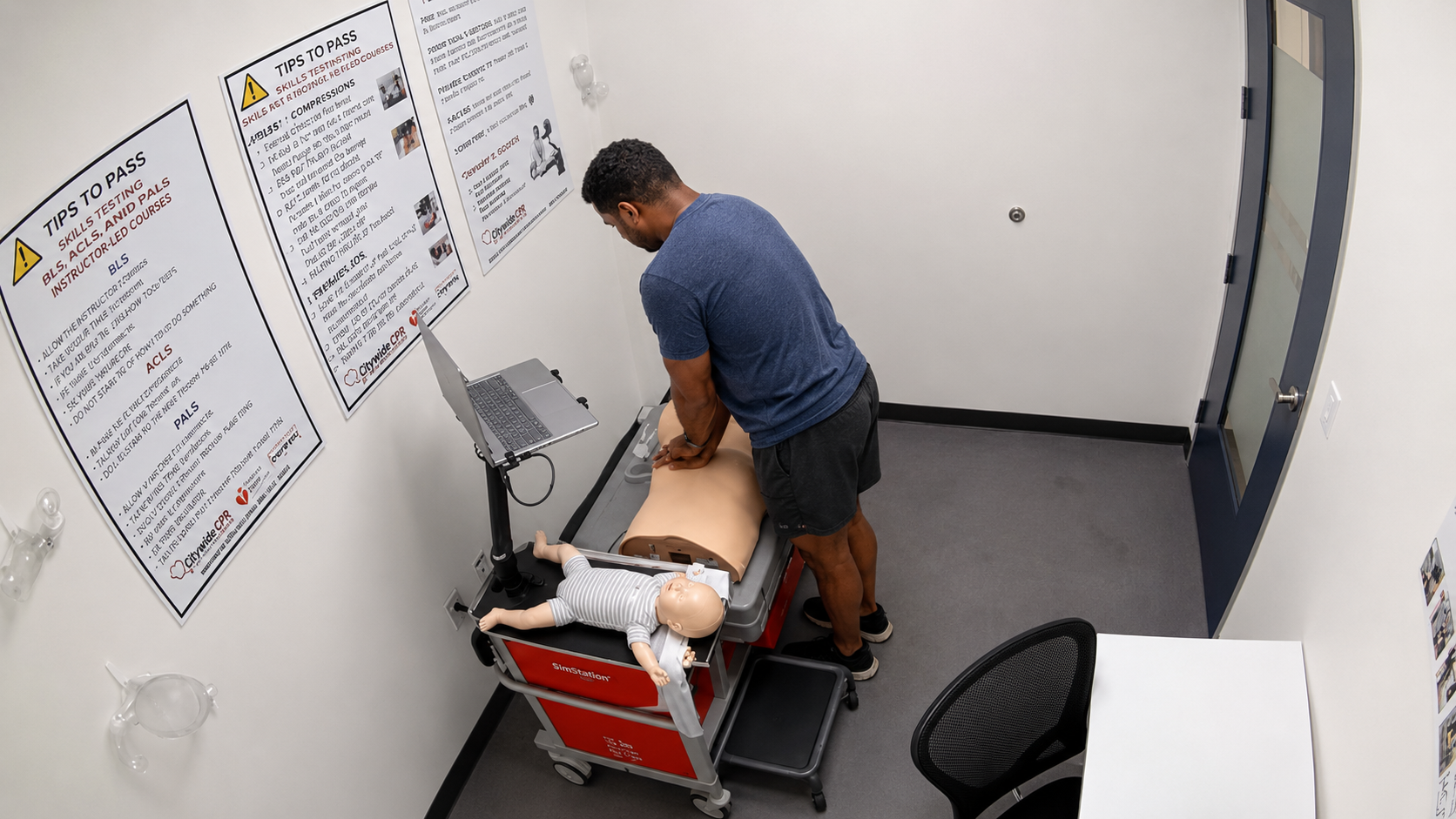 Participant performing chest compressions on an adult CPR manikin at a Citywide CPR simulation station in Charlotte, North Carolina, with an infant manikin in a onesie and laptop visible.