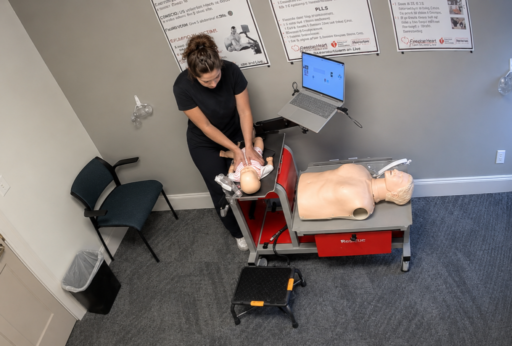 Participant performing chest compressions on an infant CPR manikin in a onesie at a Citywide CPR simulation station in Chattanooga, Tennessee, with an adult manikin and laptop visible.