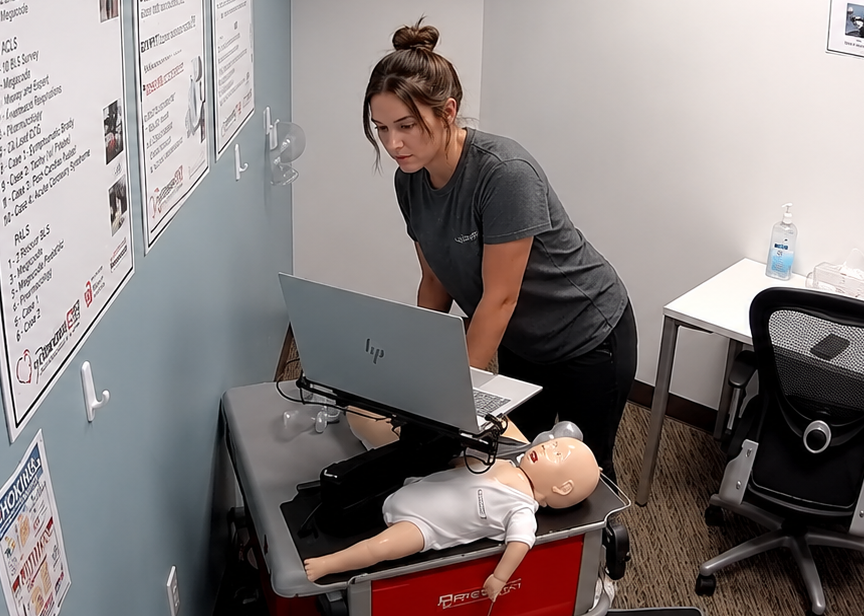 American Heart Association CPR Certification Training in Des Moines, Iowa Participant using a laptop at a Citywide CPR training station in Des Moines, Iowa, with an infant CPR manikin and training equipment visible.