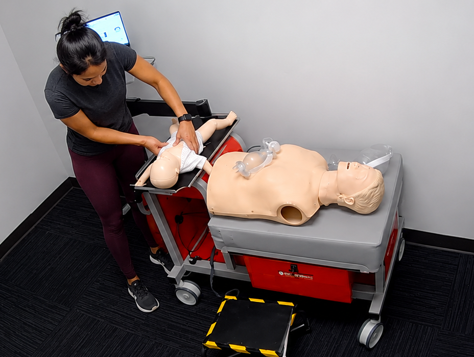 Participant practicing chest compressions on an infant CPR manikin wearing a white onesie at a Citywide CPR training station in Houston, Texas, with an adult manikin and airway equipment visible.