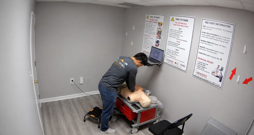 Participant performing chest compressions on an adult CPR manikin at a Citywide CPR training station in Huntsville, Alabama, with a laptop and CPR training equipment visible.