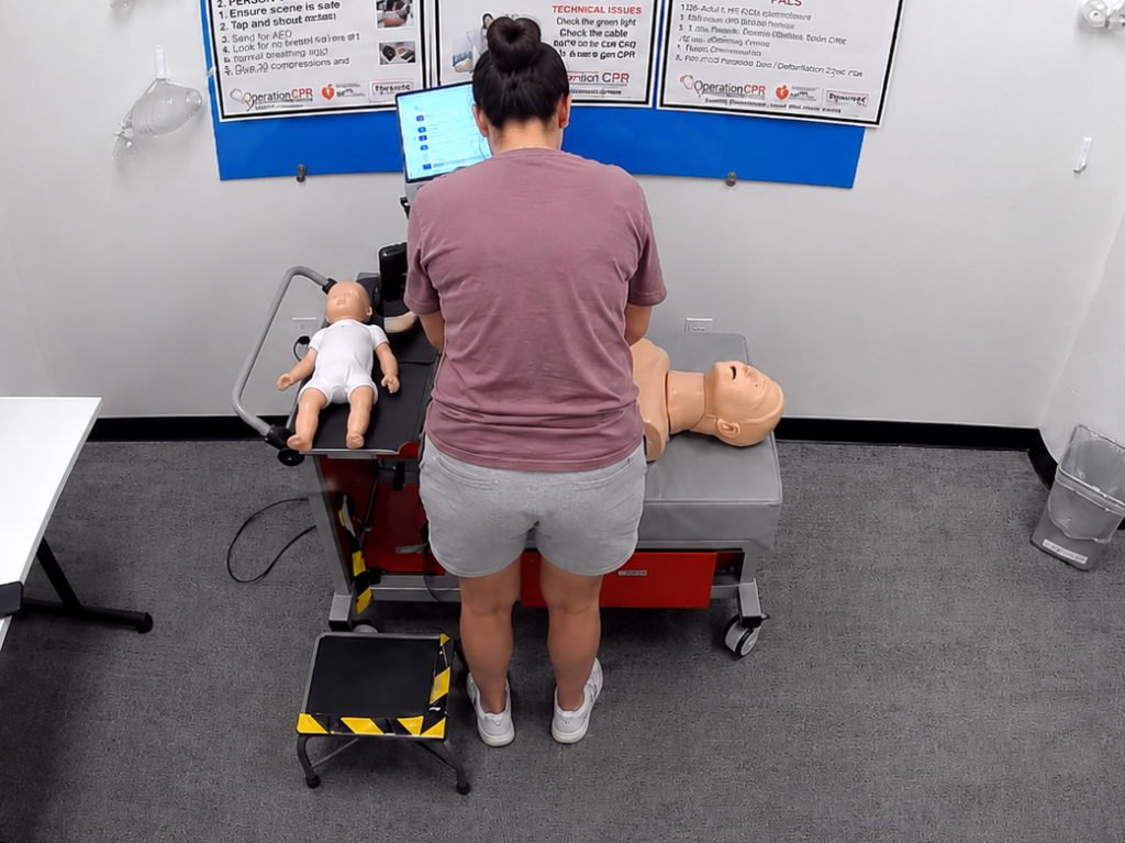 Participant standing at a Citywide CPR simulation station in River North, Chicago, with an adult CPR manikin, a fully clothed infant manikin, and a laptop visible.