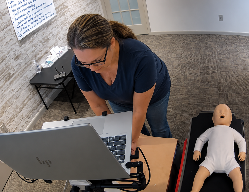 Participant providing bag-valve-mask ventilation to an adult CPR manikin at a Citywide CPR training station in Richmond, Virginia, with an infant CPR manikin wearing a white onesie and a laptop visible.