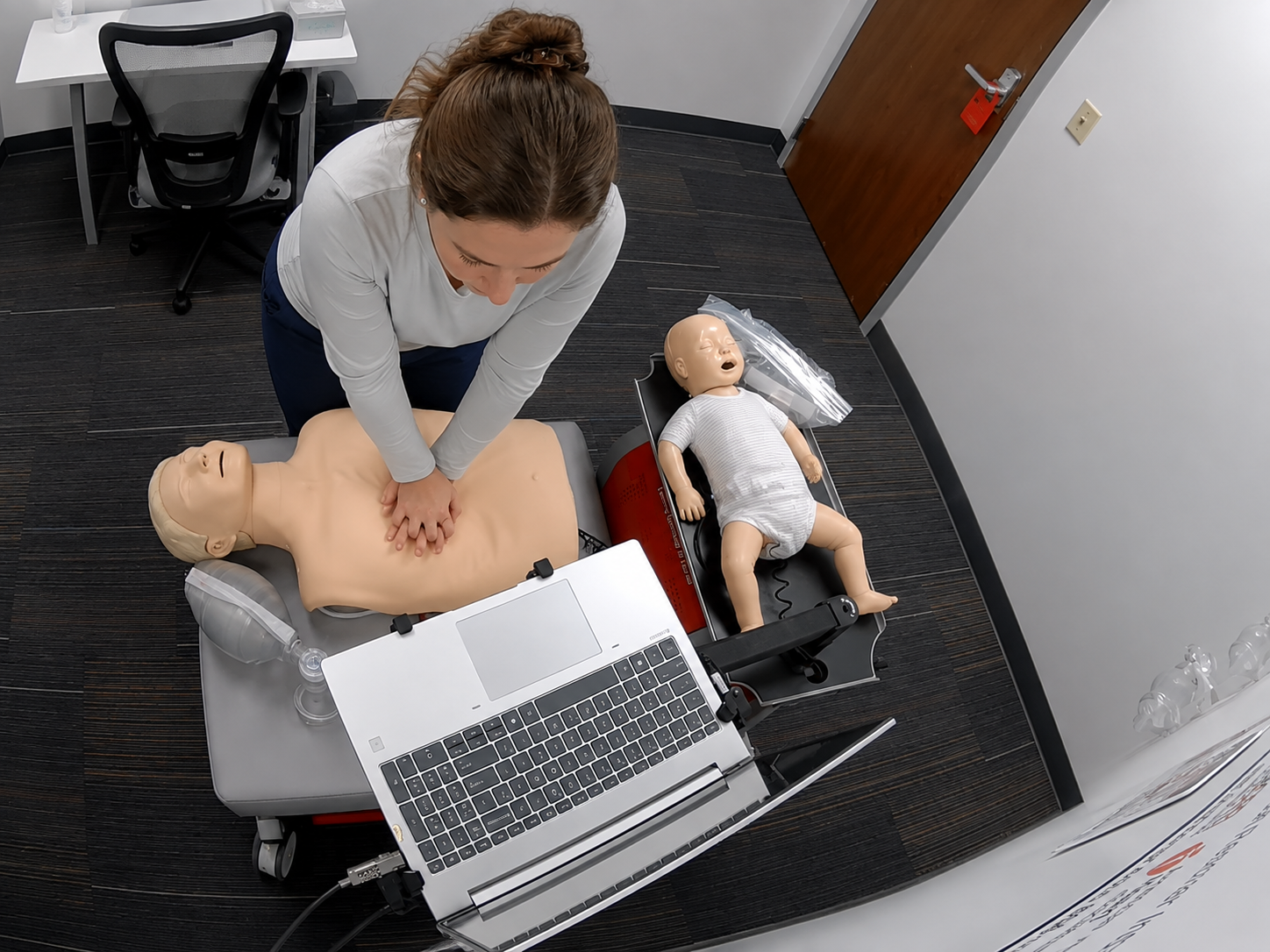 Healthcare professional performing CPR on an adult manikin during an American Heart Association BLS skills session.