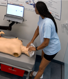 Healthcare professional performing CPR on an adult manikin at a CPR Verification Station with a training screen visible