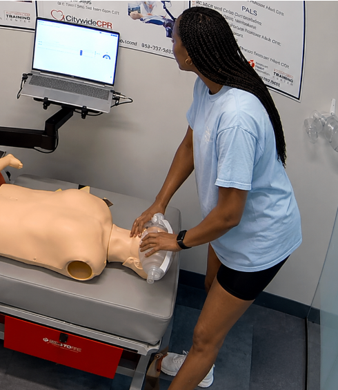 Healthcare professional performing CPR on an adult manikin at a CPR Verification Station with a training screen visible