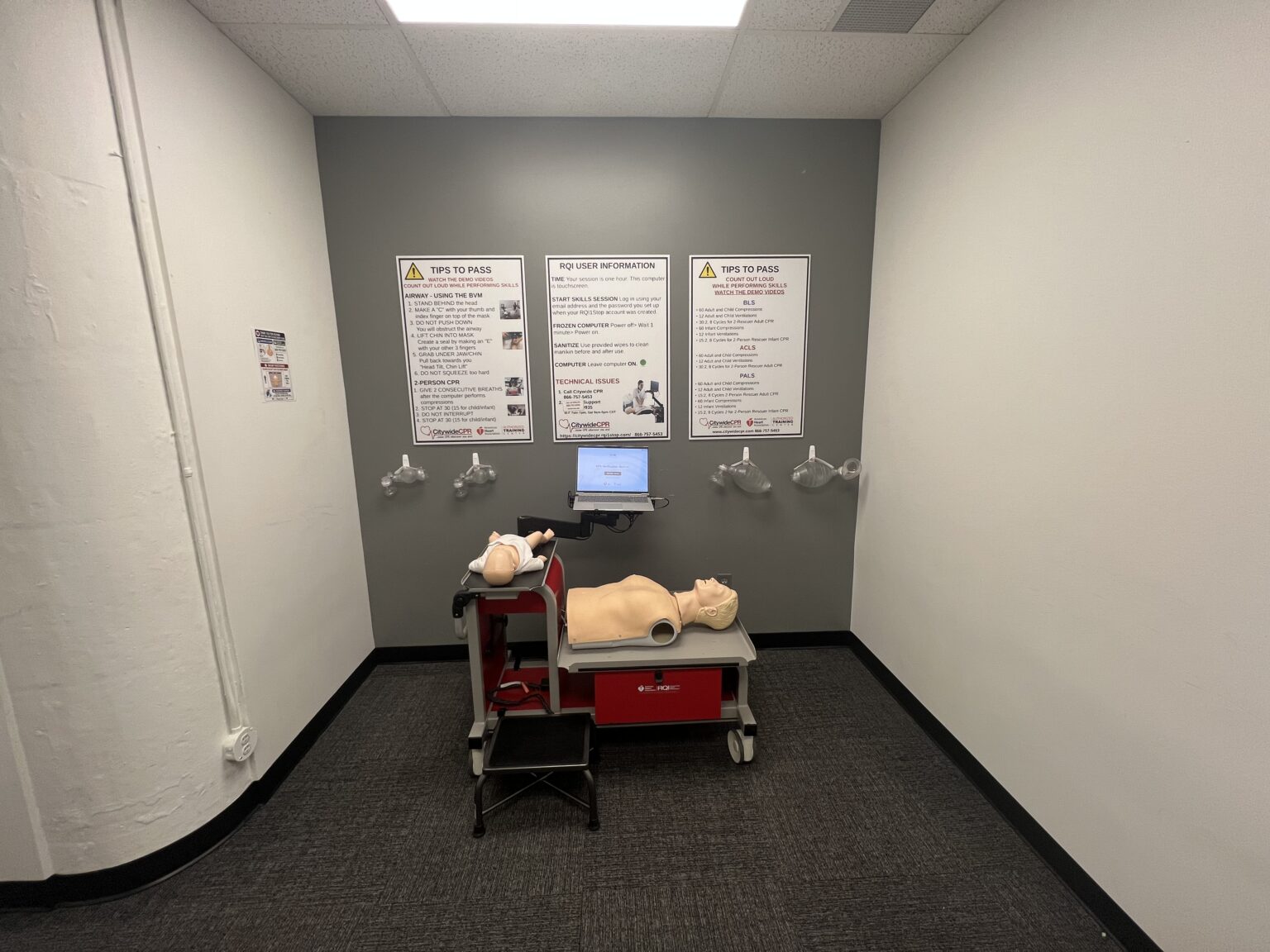 Citywide CPR Self-Guided Skills Station in Detroit, Michigan with adult and infant CPR manikins, laptop, and training posters.