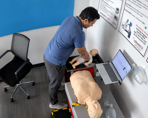 Participant practicing infant CPR chest compressions on an infant manikin at a Citywide CPR simulation station in Austin, Texas, with an adult CPR manikin and laptop visible.