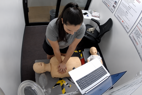 Participant performing chest compressions on an adult CPR manikin at a Citywide CPR training station in Kansas City, Missouri, with an infant CPR manikin, laptop, and CPR training equipment visible.